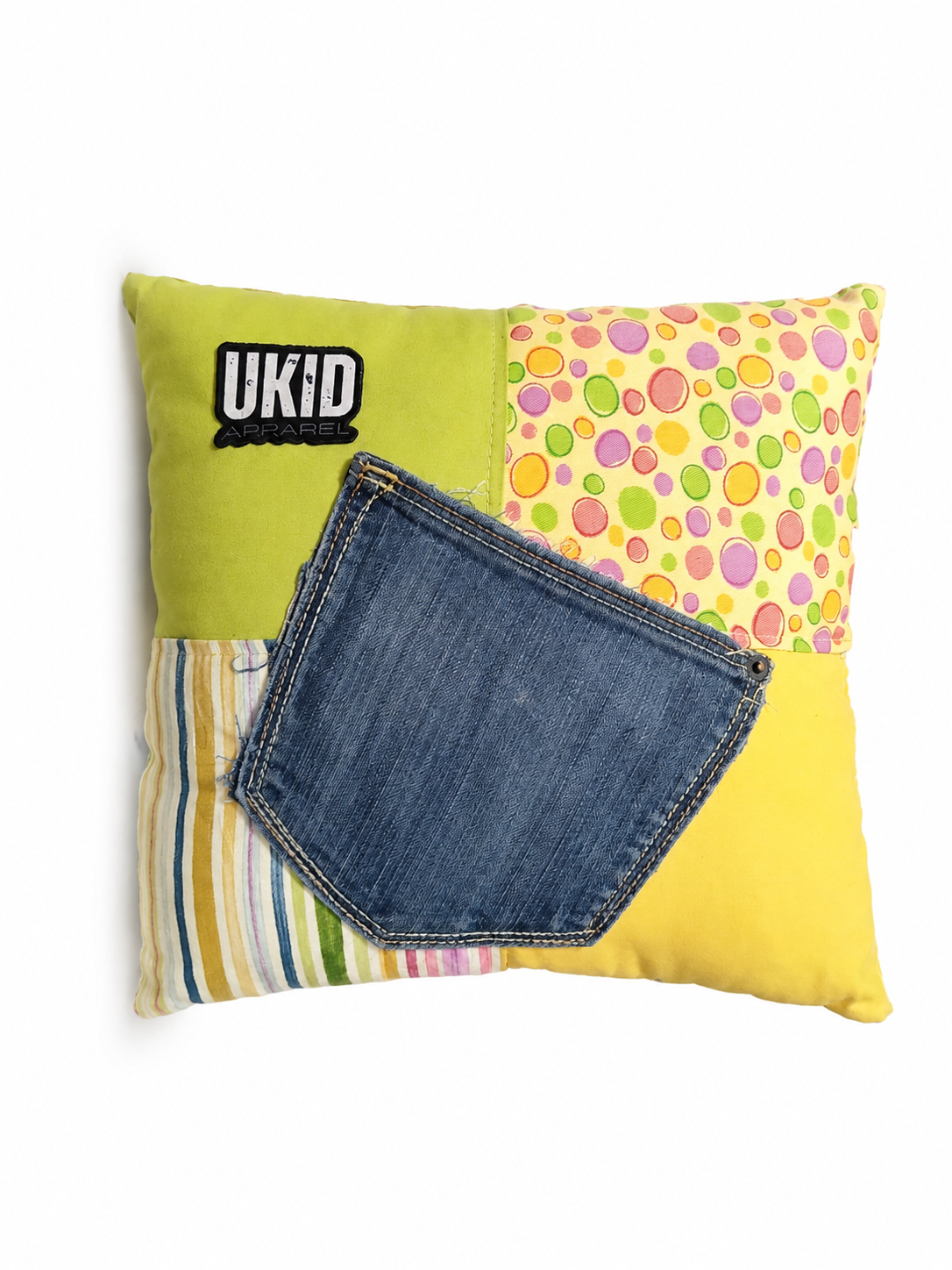 A square decorative throw pillow featuring a patchwork design with a bright yellow top-right section, a lime green bottom-left section with a black UKID logo, a colorful polka-dot pattern top-left section, a striped multicolor bottom-right section, and a large faux denim pocket detail on the front.